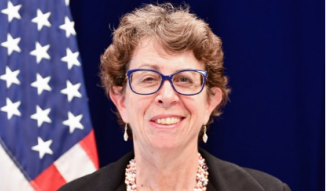 A portrait of Carolyn Glassman in front of an American flag.