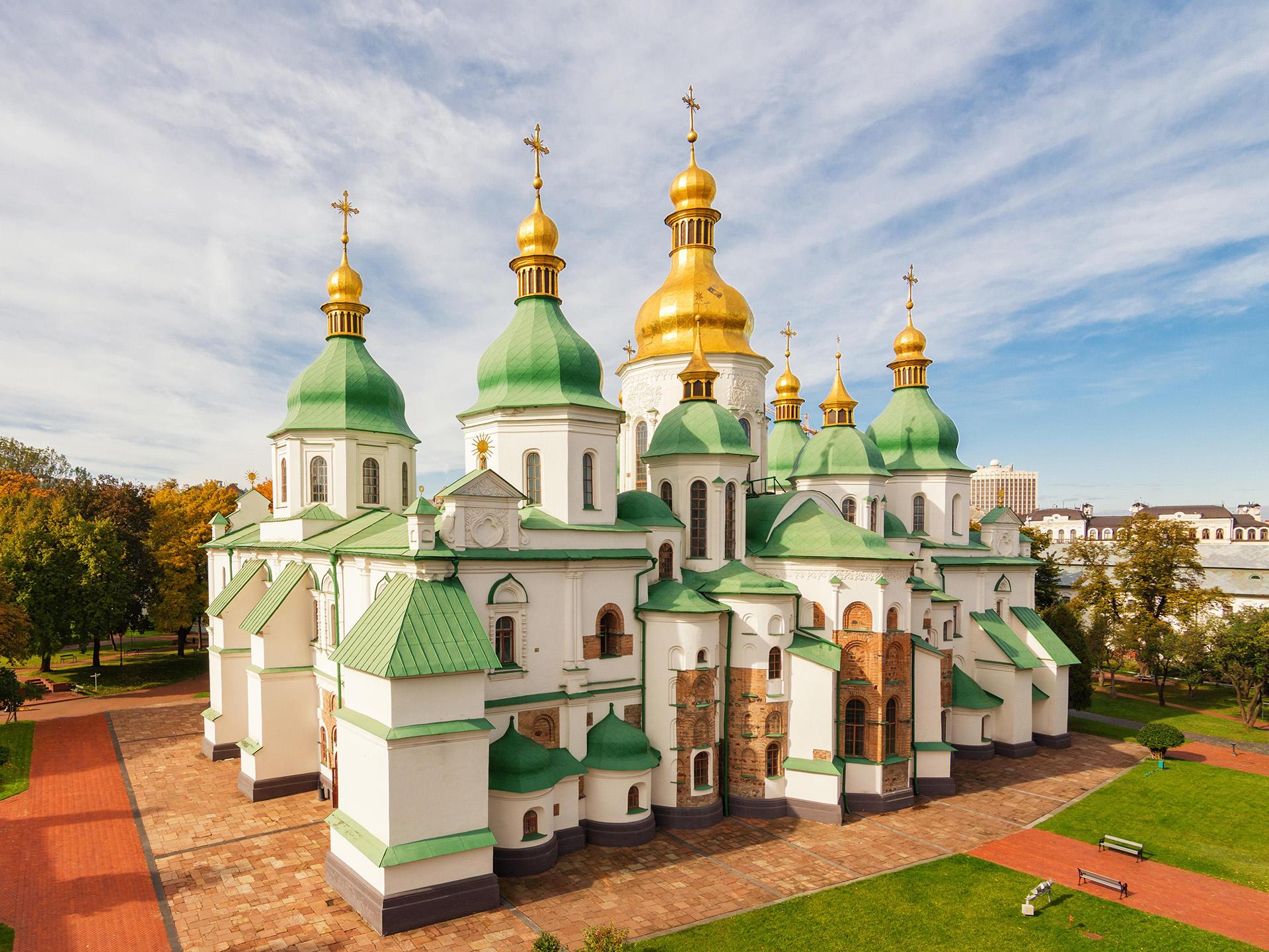 View of a Ukrainian cathedral complex with white walls, green rooftops, and gold finneals.