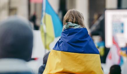 A child draped in the Ukrainian flag faces away from the camera.
