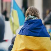 A child draped in the Ukrainian flag faces away from the camera.