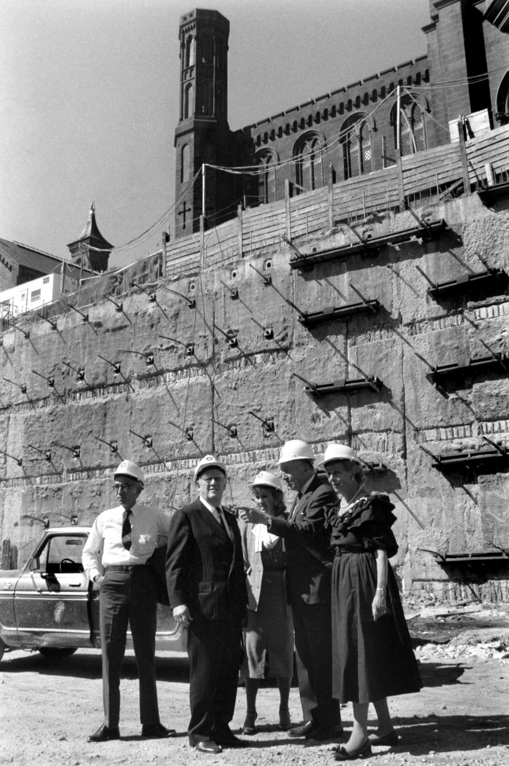 People in hard hats stand in front of construction.